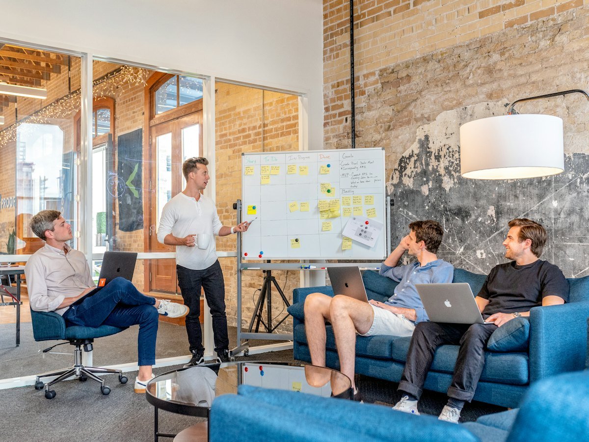 A team at laptops watching a colleague present at a whiteboard