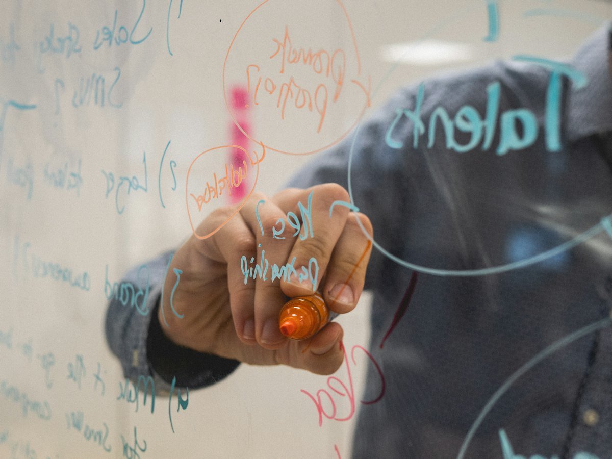 A person drawing diagrams on a glass whiteboard