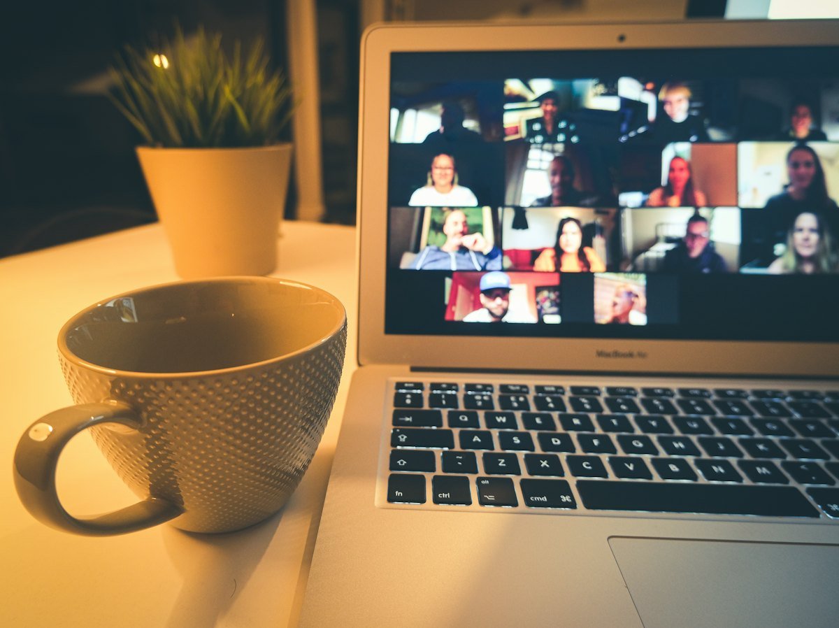 A laptop showing a video meeting beside a coffee mug