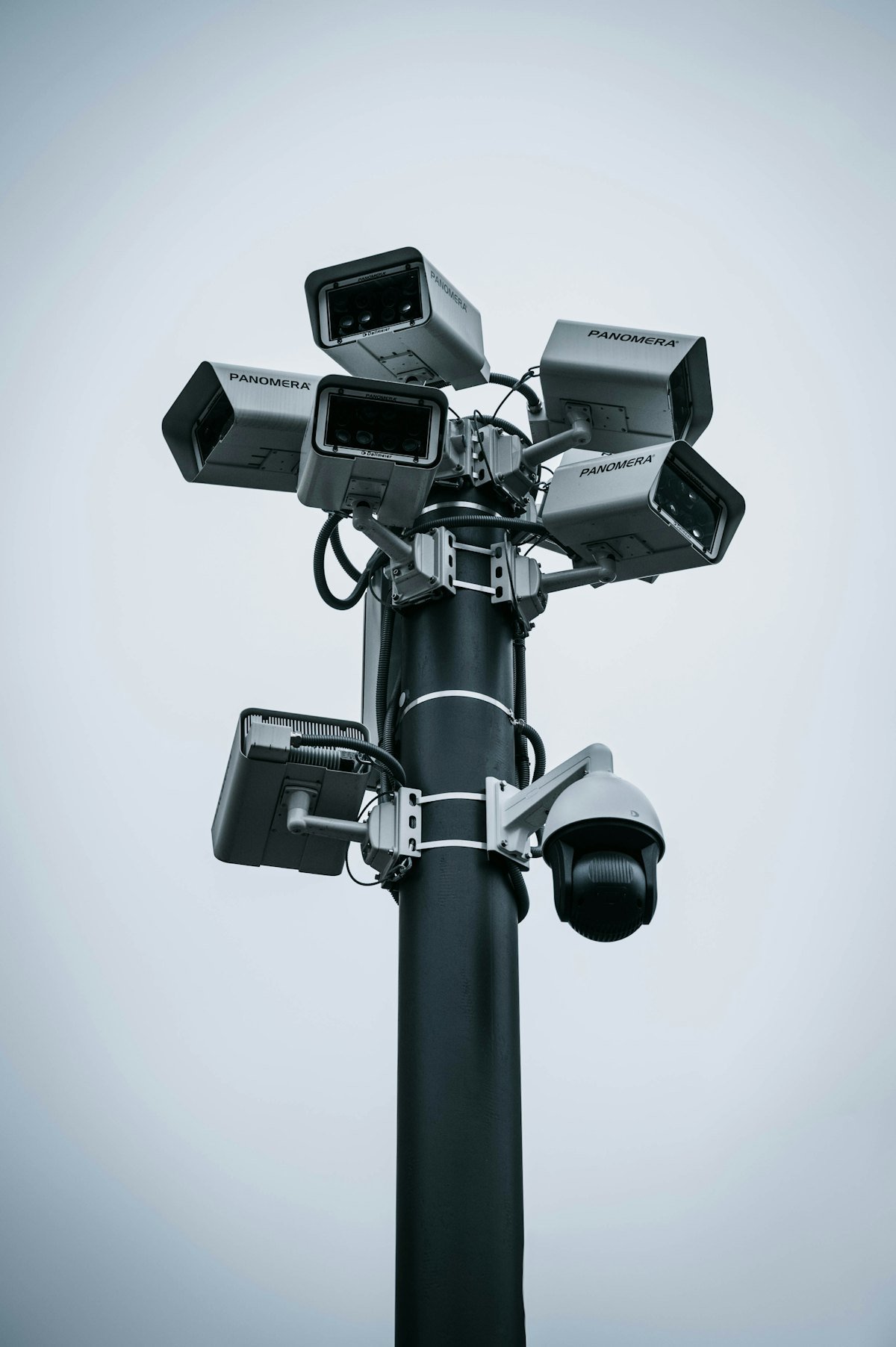 A pole of surveillance cameras against a grey sky