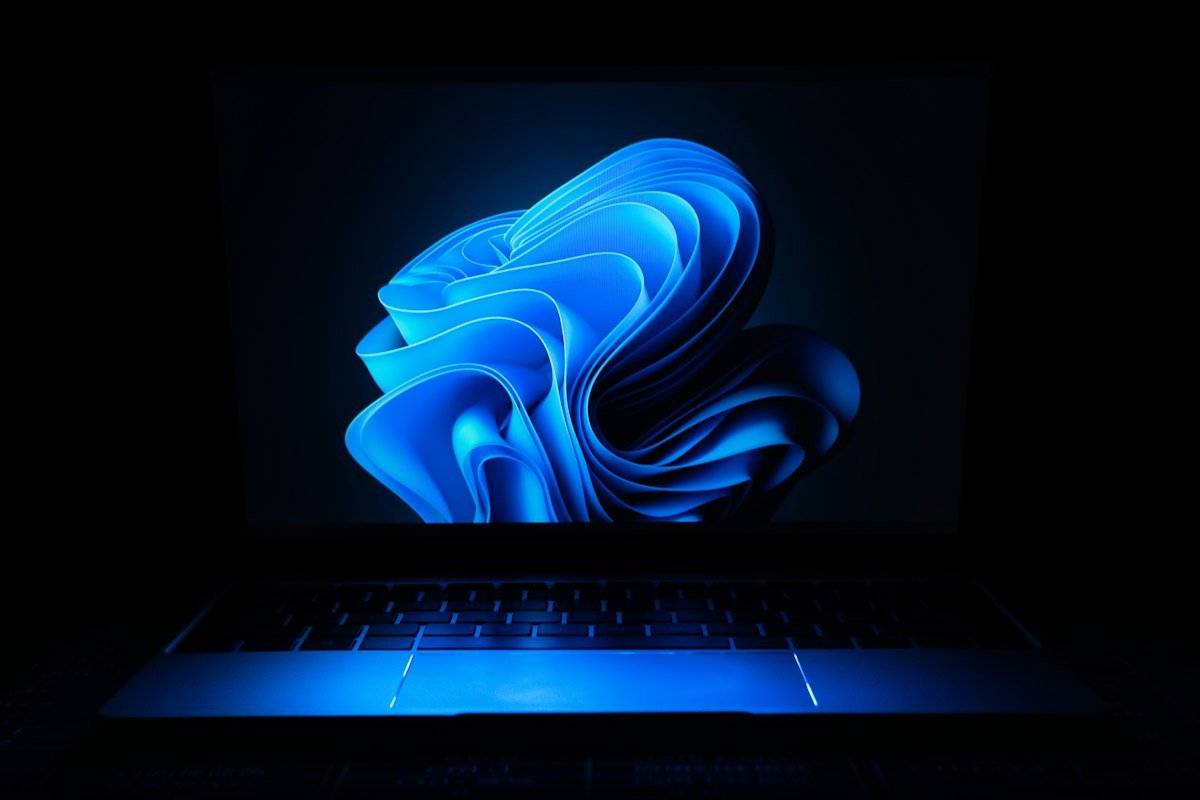 A laptop showing a blue wave wallpaper in a dark room