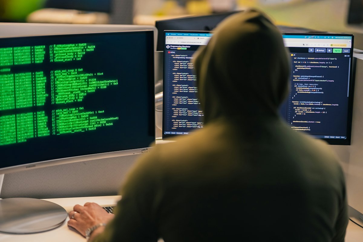 A person in a hoodie working at several computer screens